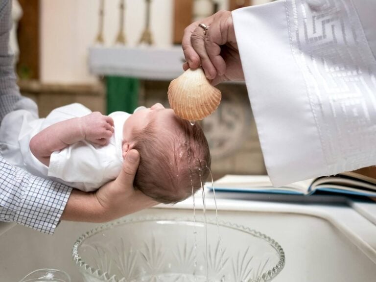 A priest baptizing a new born baby with water from a shell